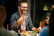 © chika_milan - Handsome caucasian bearded hipster man with eyeglasses smiling and holding glass of wine while sitting with his friends in restaurant.