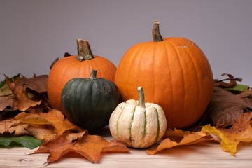 Poster - Closeup shot of pumpkins surrounded by leaves on a wooden surface getting ready for Halloween