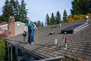 Wall Mural - Rooftop view of suburban home, mature woman with leaf blower cleaning roof and gutter