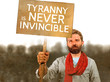© TheVisualsYouNeed - attractive hipster with scarf and beard protesting at political demonstration holding billboard with the message tyranny is never invincible defending human rights