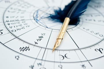 quill pen in form ob blue feather lying on horoscope and zodiac signs like astrology concept