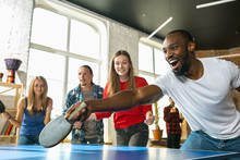 Young People Playing Table Tennis In Workplace, Having Fun. Friends In Casual Clothes Play Ping Pong Together At Sunny Day. Concept Of Leisure Activity, Sport, Friendship, Teambuilding, Teamwork.
