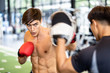 © Kawee - Soft focus shows moving action of Caucasian handsome man wearing boxing gloves punching ahead with trainer in gym or fitness club. Bear chested nice body boxing male looking forward with serious face.