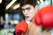 © Kawee - Caucasian handsome man wearing boxing gloves punching ahead with one fist to camera in gym or fitness club. The bear chested nice body boxing male looking forward with serious face. Fitness for health