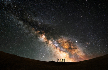 Wall Mural - Silhouette of a group of people standing on a hill. Behind them is the beautiful bright Milky Way Galaxy.