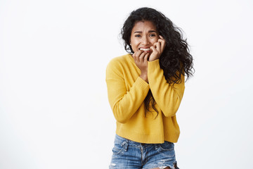 Wall Mural - Terrified, scared young african american woman in yellow sweater, biting fingers, frowning and touching face from fear, stopping afraid stare camera frightened, standing white background