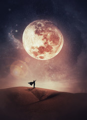 surreal scene with a woman hero silhouette with cape on the top of a hill raises hand up to the sky 