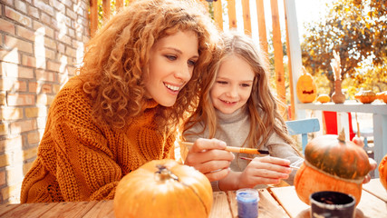 Happy woman drawing on pumpkin with her little daughter