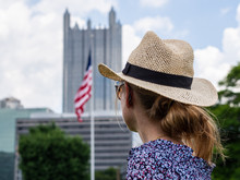 Woman With Blonde Hair And Beige Hat Looking At The Skyscraper At PPG Place With American Flag In Downtown Pittsburgh.