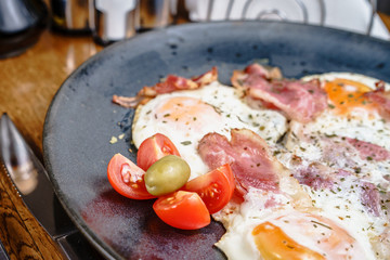 Wall Mural - Bacon or ham and eggs in a plate by the fork knife and bread ready to eat served on the table