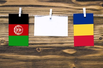 Wall Mural - Hanging flags of Afghanistan and Romania attached to rope with clothes pins with copy space on white note paper on wooden background.Diplomatic relations between countries. Cooperation concept.