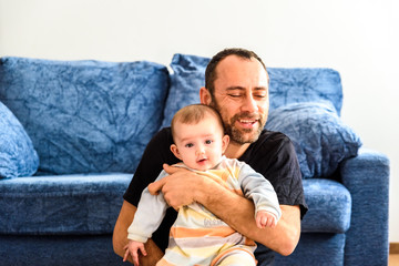 Wall Mural - Father sitting on the floor with his baby in his arms in the living room of home.