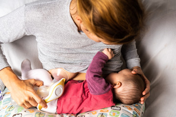 Mother breastfeeding her newborn baby while using a manual breast pump.