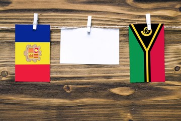 Hanging flags of Andorra and Vanuatu attached to rope with clothes pins with copy space on white note paper on wooden background.Diplomatic relations between countries.