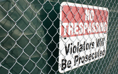 No trespassing signboard covered by metal grid on the street wall and on the darck background.Urban life, textured background.