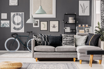 Wall Mural - Wicker pouf on the floor of grey inspiring living room interior with bike, corner sofa and posters on the wall