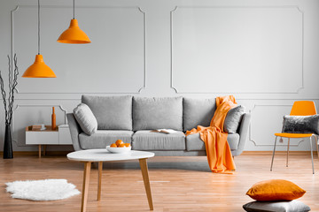 orange lamp above grey scandinavian sofa in modern interior