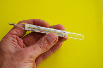 Man hold in hand tool for measuring human body temperature in colds and flu at home and in the hospital. Glass flask with a capillary that contains mercury on yellow background.