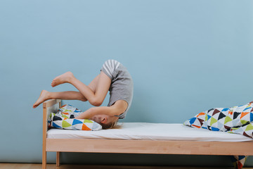 Little boy doing morning gymnastics in unmade bed. Forward roll exercise.