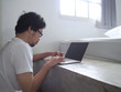 © tuaindeed - Young Asian man using computer laptop in living room. Internet of things