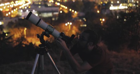 Wall Mural - astronomer with a telescope watching at the stars and moon with blurred city lights in the backgroun