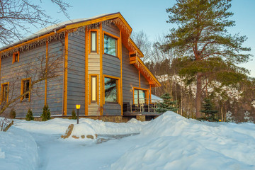 Two-storey cottage on the background of pine. Country house with garlands. Winter holidays in the village. Christmas holiday in nature. Get out of town for the holidays.