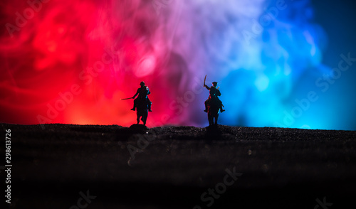 Obraz Dibond World war officer (or warrior) rider on horse with a sword ready to fight and soldiers on a dark foggy toned background. Battle scene battlefield of fighting soldiers.