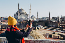 Young European Woman Takes A Selfie Portrait In Istanbul, Turkey. Girl Walks Through Winter Istanbul. Blonde Takes A Photo On The Phone Against The Background Of A Mosque In Autumn Day.