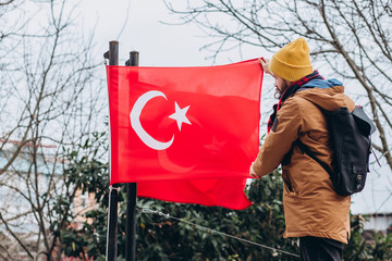 A guy in a yellow hat is photographed in a park with the flag of Turkey in the winter. A tourist walks through the autumn park in Istanbul.