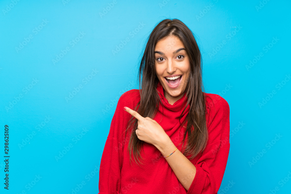 Young woman with red sweater over isolated blue background pointing finger to the side - obrazy, fototapety, plakaty 