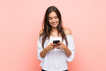 Young woman over isolated pink background sending a message with the mobile