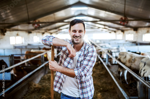 Cuadros en Lienzo Handsome smiling caucasian farmer leaning on hay fork and looking at camera