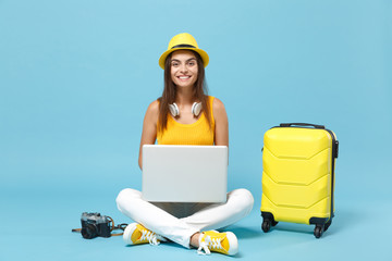 Traveler tourist woman in yellow casual clothes, hat with suitcase laptop pc photo camera isolated on blue background. Female passenger traveling abroad travel on weekends. Air flight journey concept.