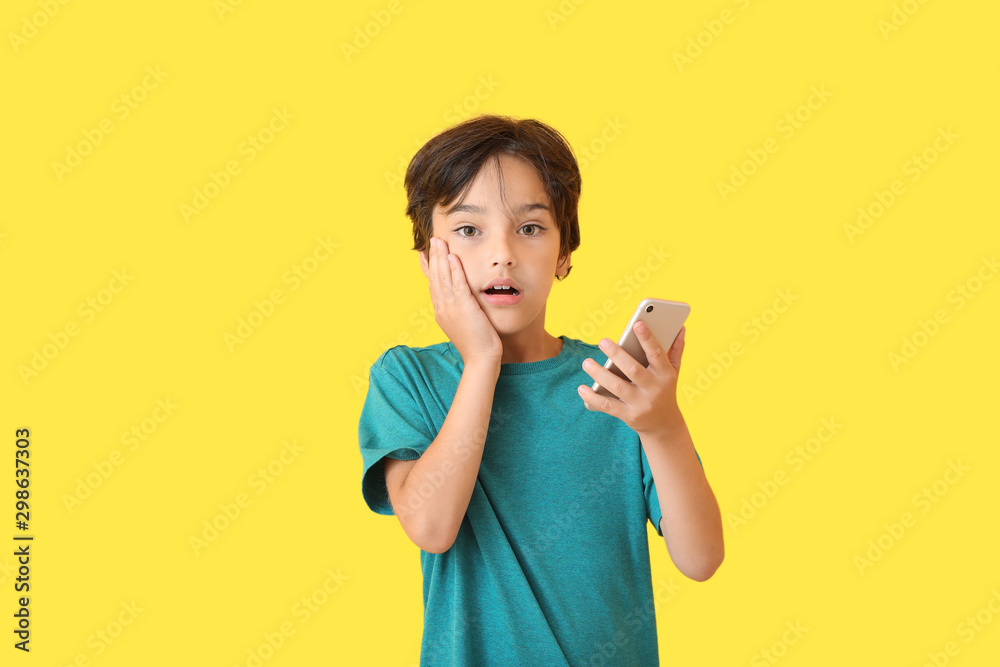 Surprised little boy with mobile phone on color background