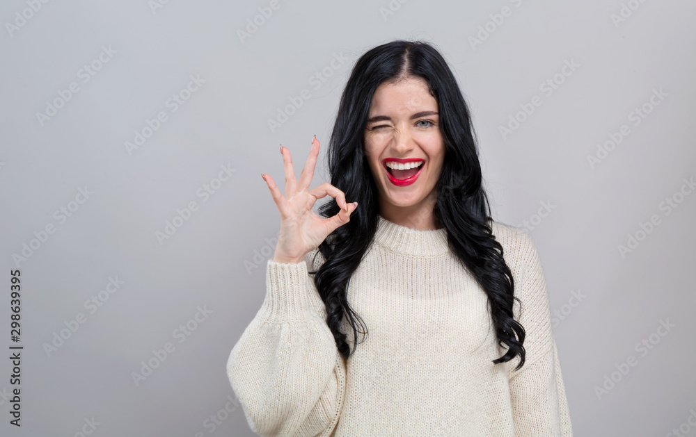 Young woman with ok gesture on a gray background - obrazy, fototapety, plakaty 