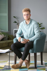 Sticker - Portrait of stylish young man with cup of coffee resting at home