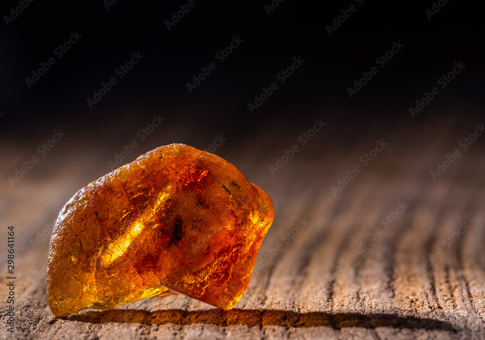 Natural amber. A piece of yellow transparent natural amber on large piece of dark stoned wood. - obrazy, fototapety, plakaty 