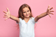 canvas print picture - cheerful positive beautiful girl in white t-shirt with arms wide open looking at the camera, kid meeting her guests, welcome, kindness, friendship. close up portrait, isolated pink background