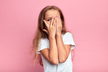 Emotional Little Girl Covers Her Face With Her Hand Isolated Over Pink Background, Child Watching Horror Film, Movie, Reaction, Facial Expression. Isolated Pink Background