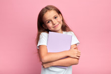 Little Beautiful Smiling Girl Holding Book, Going To School. Close Up Portrait, Isolated Pink Background, Childhood. Kid Hugging A Book. Lifestyle, Interest, Hobby, Free Time, Spare Time