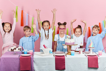 happy attractive children with raised arms having fun in the studio, happiness, positive feeling and emotion, isolated pink background