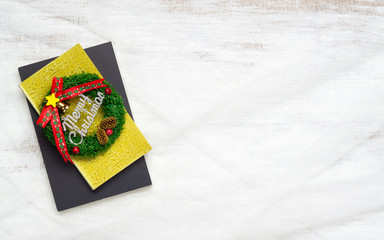 Merry Christmas sign on notebook on nest fabric on white wooden board. Minimal flat lay top view with copy space.