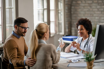 Smiling African American doctor advising a couple about taking pills during medical appointment.