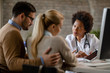 © Drazen - African American female doctor using touchpad while talking to a couple at clinic.
