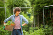 © mimagephotos - female farmer smiling with bunch of vegetables in basket by garden