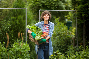 Wall Mural - female farmer smiling with bunch of vegetables in basket by farm