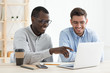African guy pointing to data on laptop for his European colleague while working together on business project
