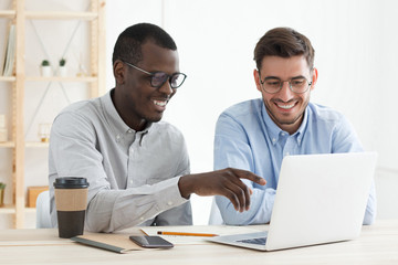 african guy pointing to data on laptop for his european colleague while working together on business