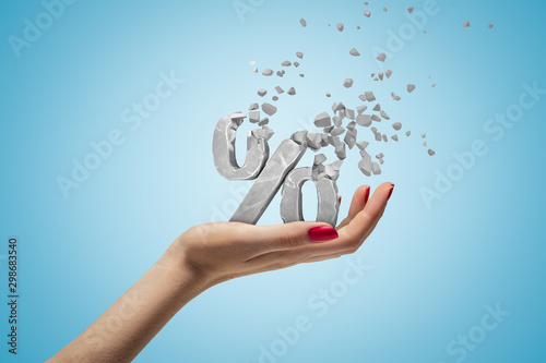 Cuadros en Lienzo Closeup of woman's hand holding percent sign which is breaking into small pieces that are flying away on light blue background