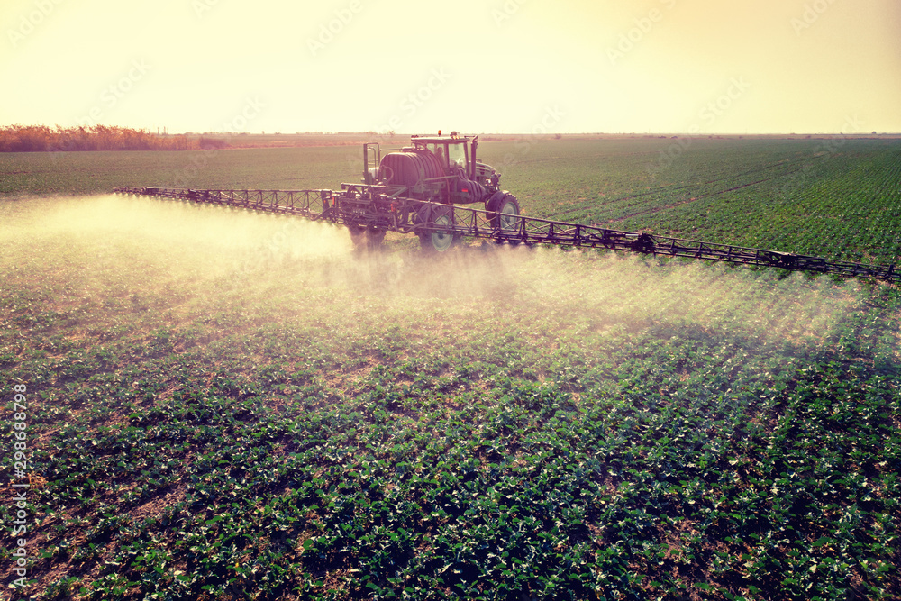 Tractor spraying fertilizer or pesticides on field with sprayer - obrazy, fototapety, plakaty 